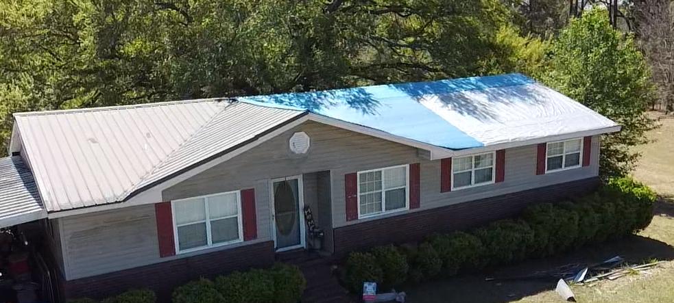 Single-story home with blue tarp covering damaged roof and red shutters