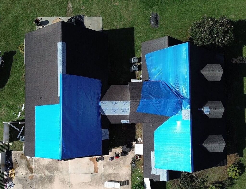Aerial view of house roof replacement with blue tarps covering damaged sections