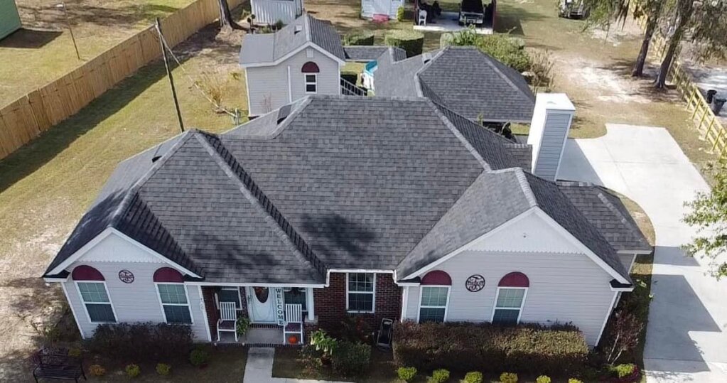 Aerial view of single-story white brick home with gray shingle roof and red accents
