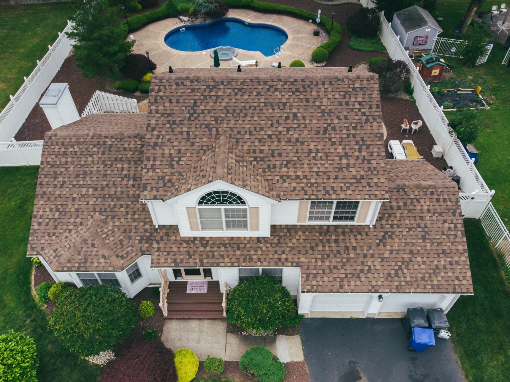 Aerial view of white suburban house with brown shingle roof and backyard pool
