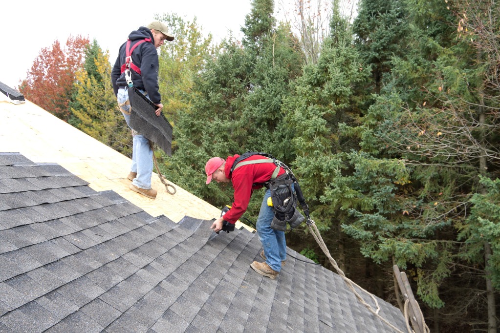 Workers installing shingles on roof.
