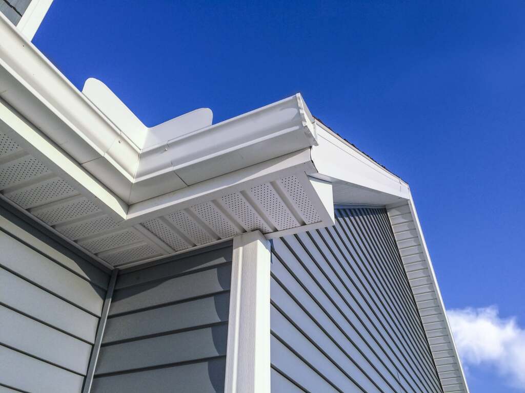 White vinyl siding house corner with soffit and fascia against bright blue sky