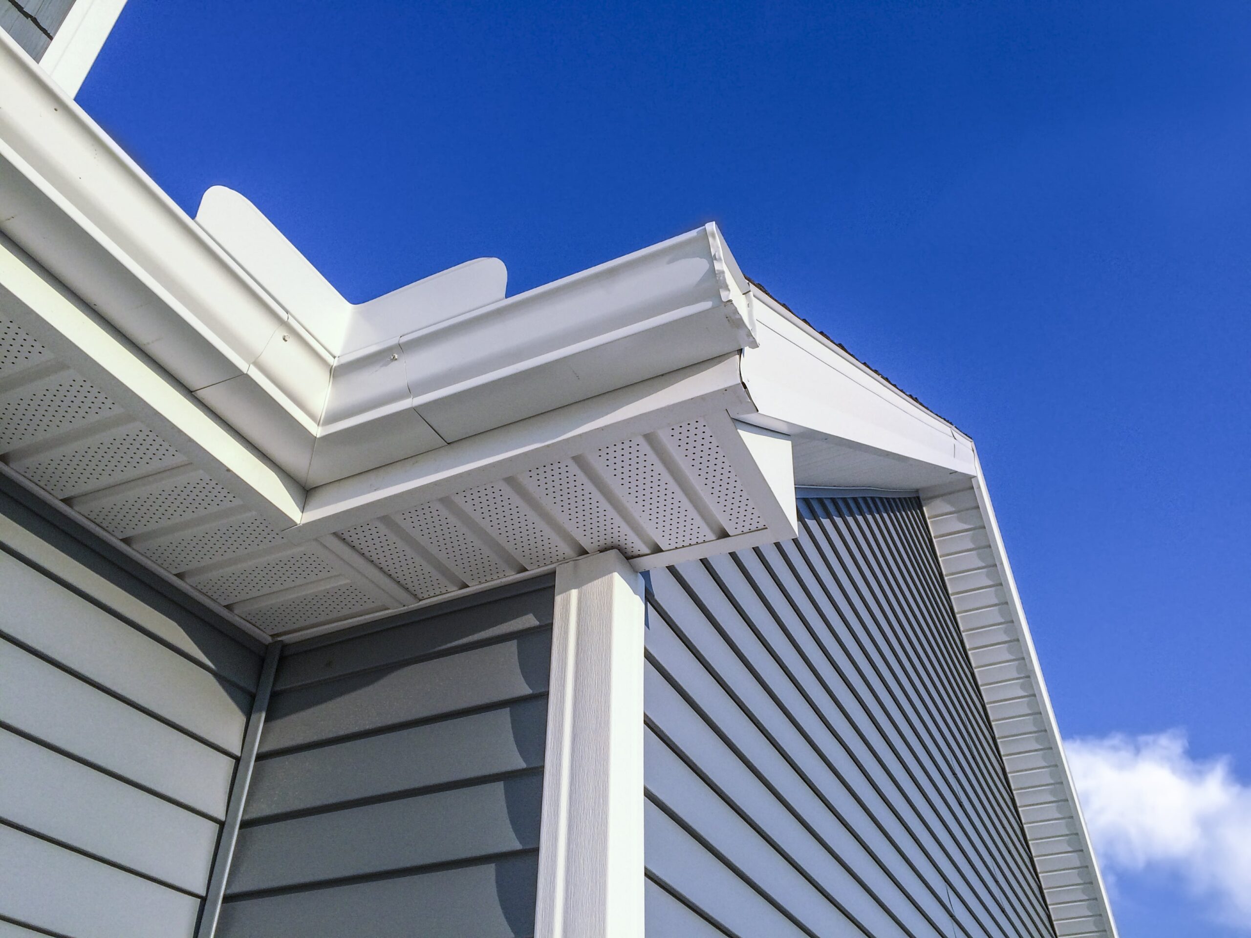 White vinyl siding house corner with soffit and fascia against bright blue sky