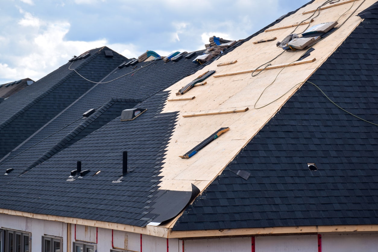 Damaged residential roof with missing shingles exposing plywood decking beneath