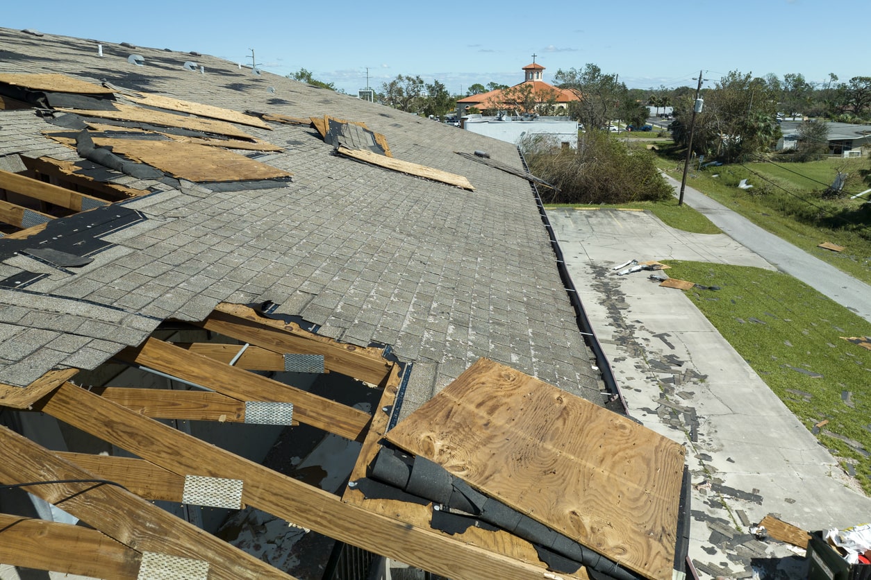 Storm damaged house roof with missing shingles and exposed wooden beams