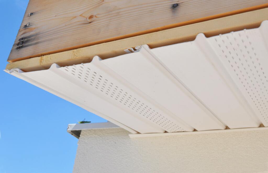 White perforated soffit panels installed under roof eaves with exposed wood rafters