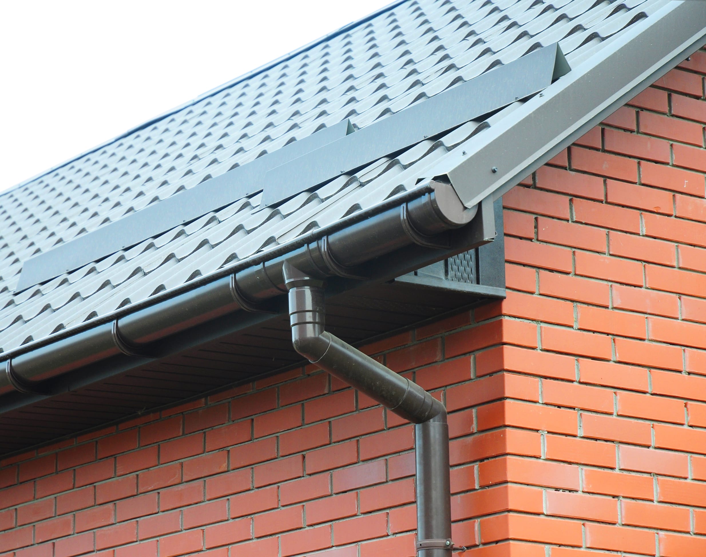 Dark brown rain gutter and downspout system on brick house with gray roof tiles