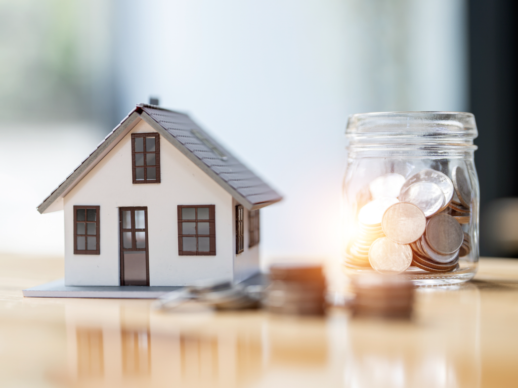 Miniature house model beside glass jar filled with coins on table