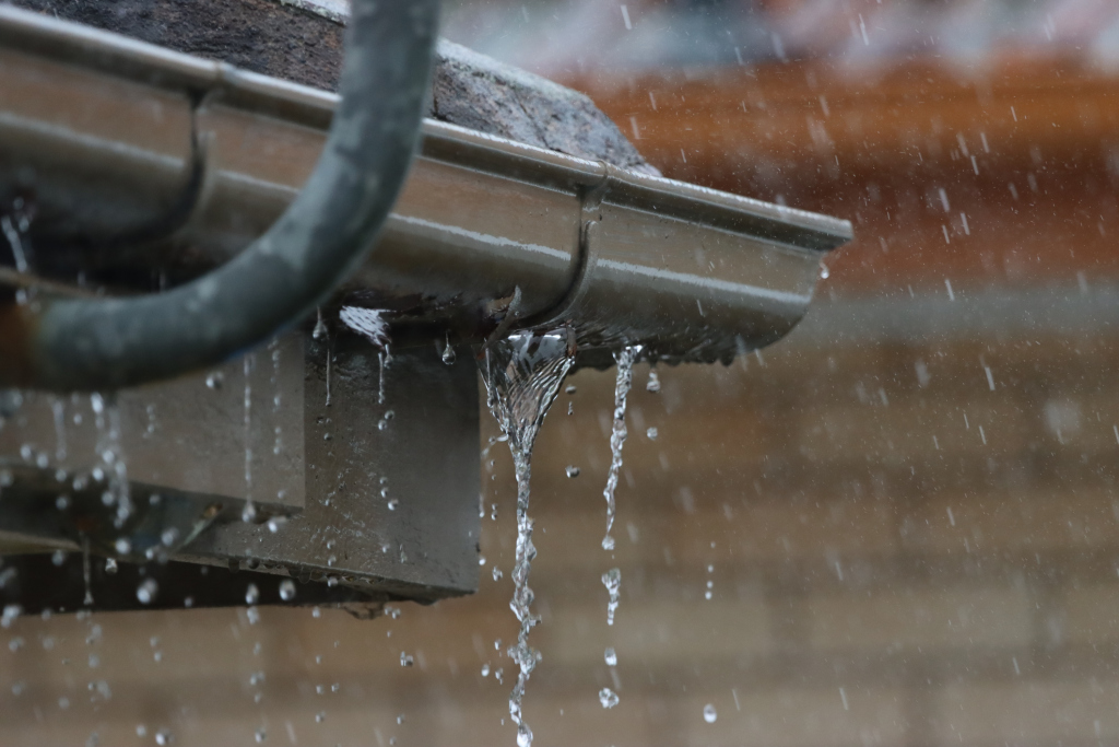 Rainwater flowing from metal roof gutter downspout during heavy rainfall storm