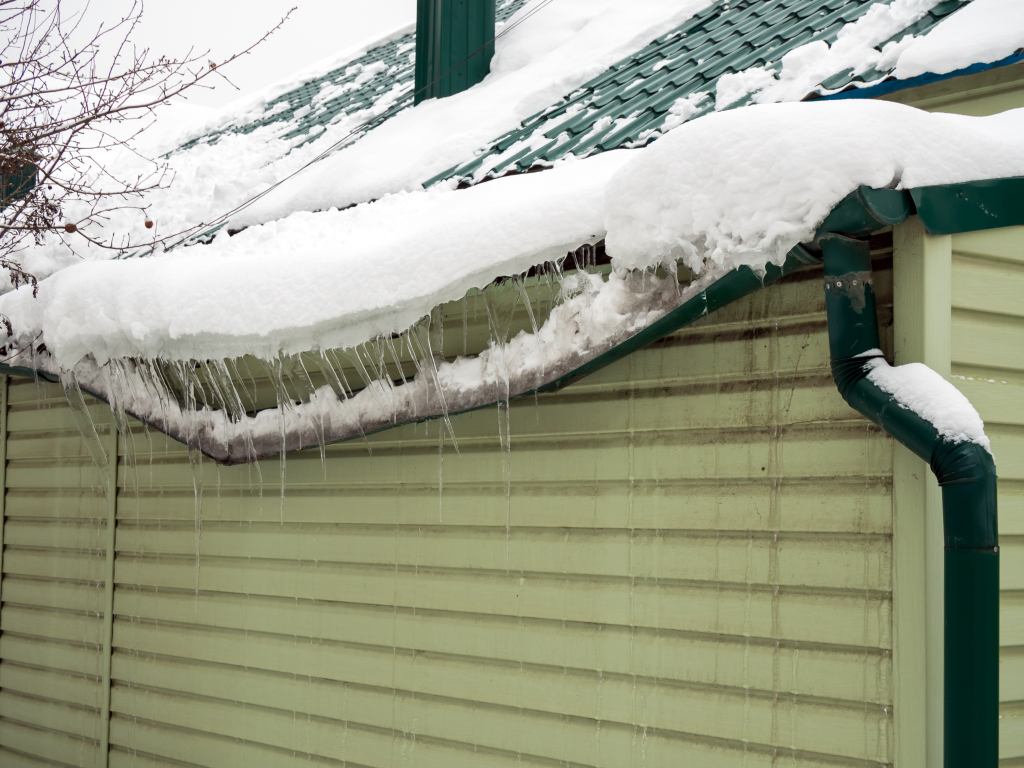 Heavy snow and icicles on house roof with green gutters during winter storm