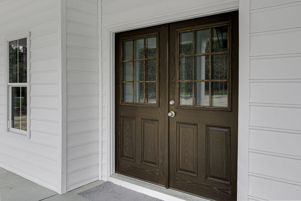Elegant wooden front doors with window panels on a white house exterior.