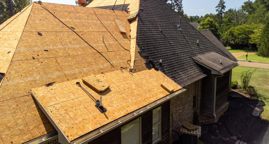 Aerial view of house roof replacement showing new plywood sheathing and existing shingles