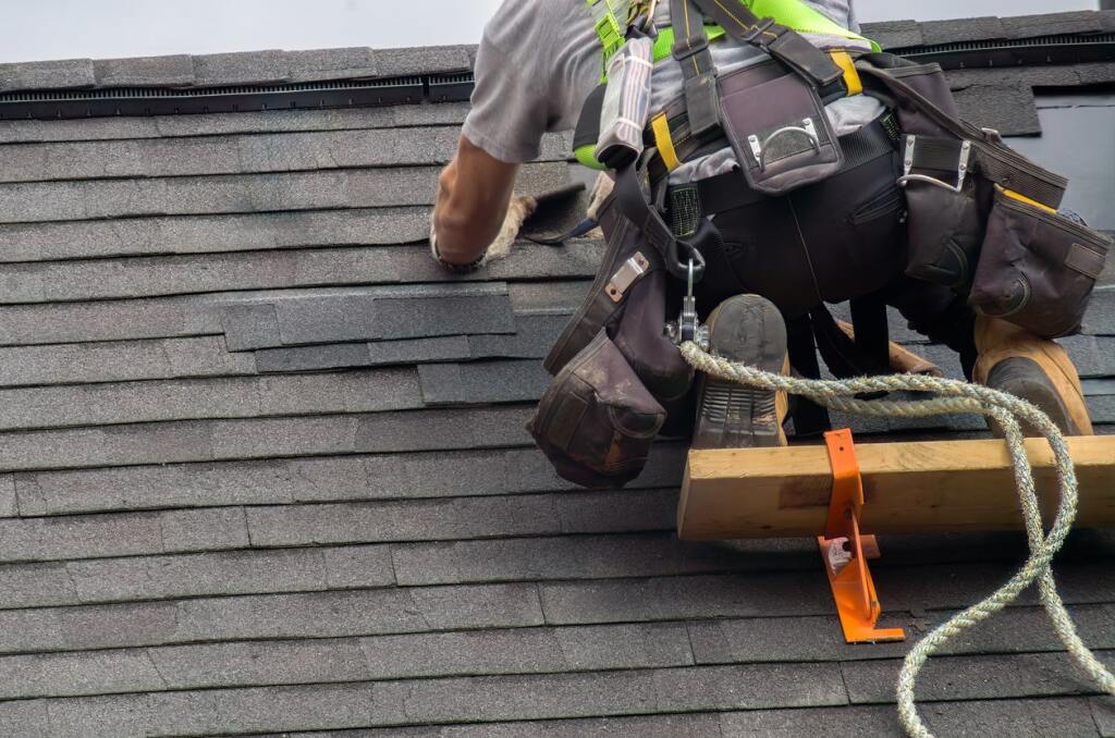 Worker repairing roof shingles safely.